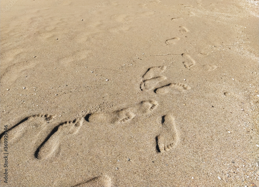 Many different prints of male and female legs on the sea sand with sea shells. Walk barefoot along the shore with footprints. Tourist rest. Many different prints of male and female legs on the sea sand with sea shells. Walk barefoot along the shore with footprints. Tourist rest.