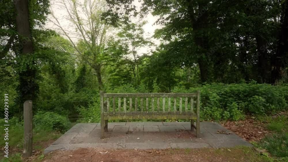 Drone push-in towards an old, empty, wooden park bench that overlooks a lush forest Drone push-in towards an old, empty, wooden park bench that overlooks a lush forest