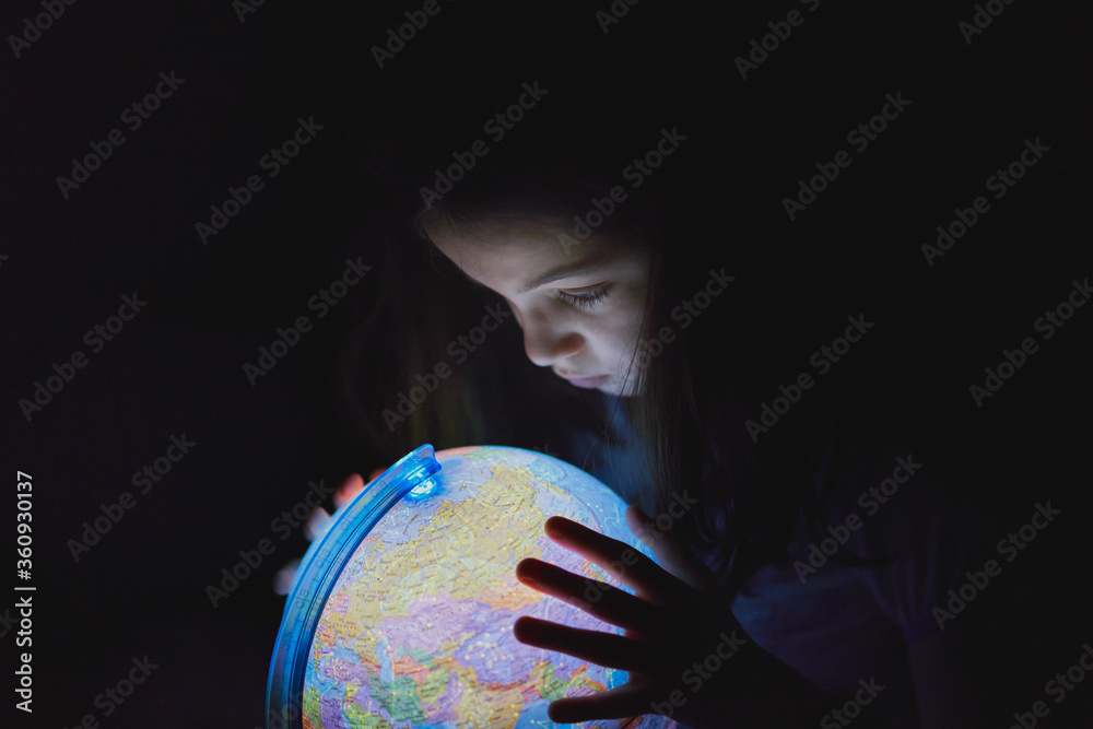 Fototapeta premium Little girl looking in the dark at an illuminated earth globe