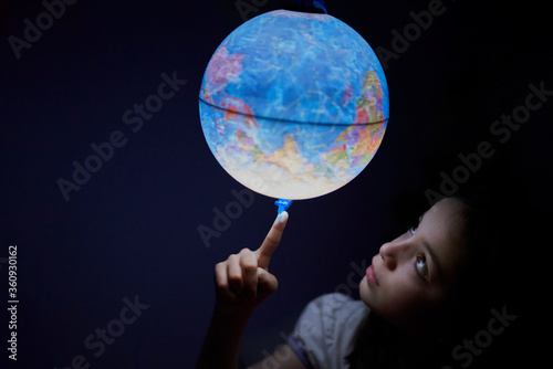 Little girl looking in the dark at an illuminated earth globe
