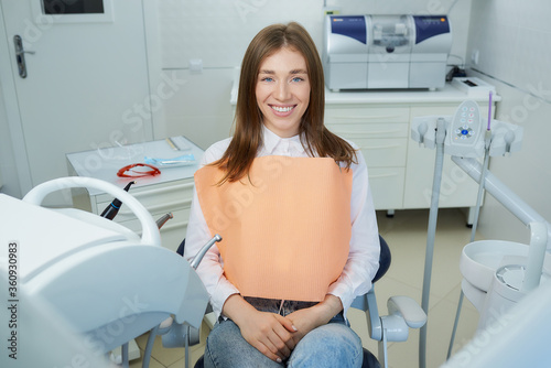A pretty young woman is sitting in the dental chair. A female patient is demonstrating her excellent smile after treatment in a dentist s office.