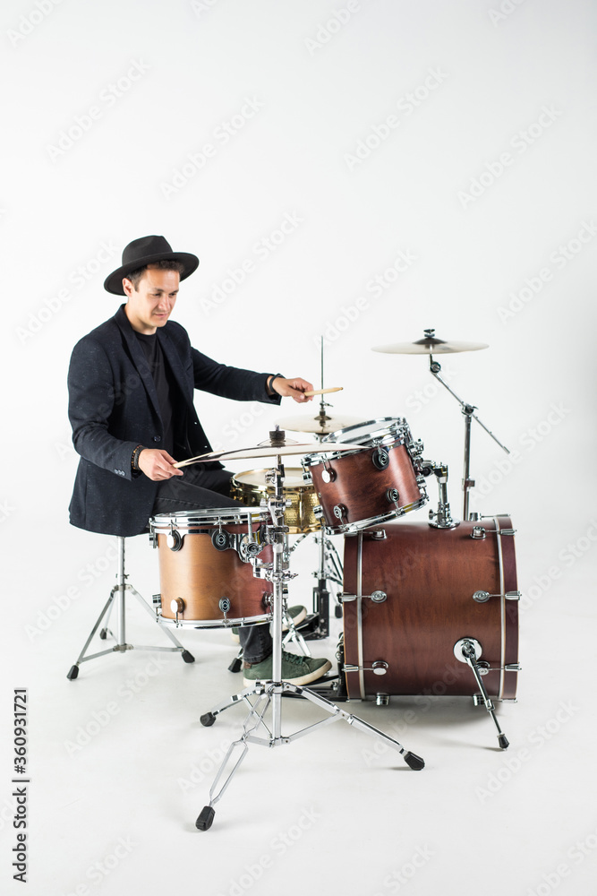 Fototapeta premium Young man drummer behind drum set and plays the drums in studio background