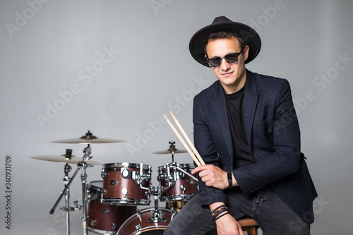 Fototapet Young man drummer behind drum set and plays the drums in studio background
