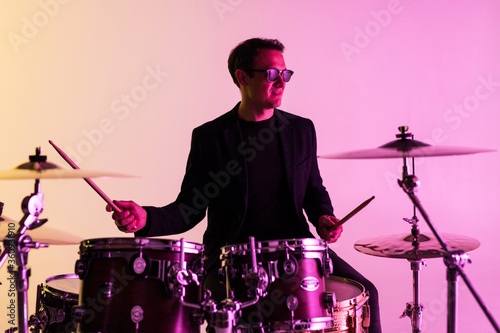 Caucasian male drummer improvising isolated on light studio background in neon light Fototapeta