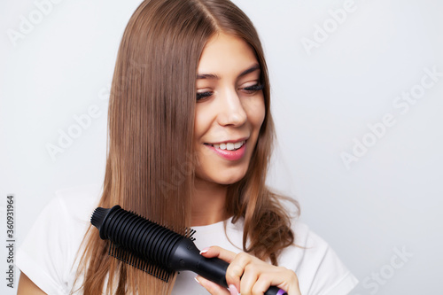 Beautiful young woman uses a hair straightener to make a beautiful styling