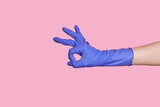 A hand in a latex surgical blue glove makes an ok gesture. on pink background
