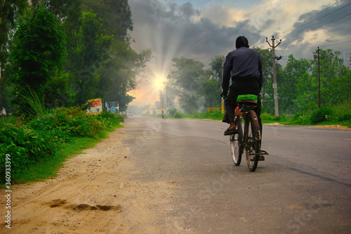 An indian laborer going home after work in bicycle towards a sunset