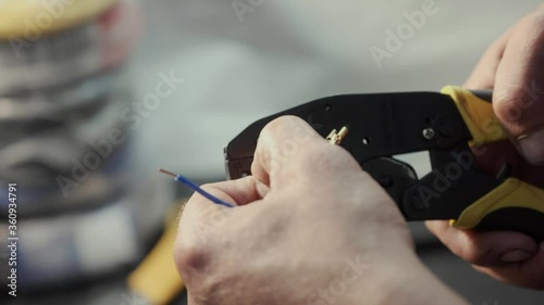 skilled technician puts small connectors to bright color thin wires using crimping tool on blurred background in workshop close view
