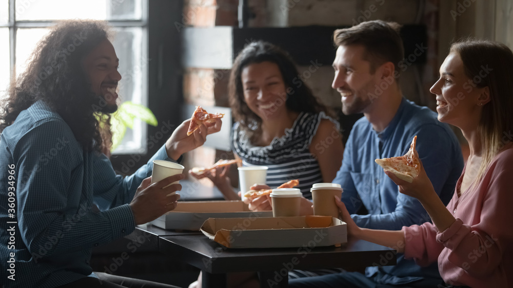 Mixed-race caucasian friends sit at table in cafe eat pizza drink coffee having funny talk. Sharing ordered pizza slices spend Friday in pizzeria yummy fast food. Racial equality, friendship concept Mixed-race caucasian friends sit at table in cafe eat pizza drink coffee having funny talk. Sharing ordered pizza slices spend Friday in pizzeria yummy fast food. Racial equality, friendship concept