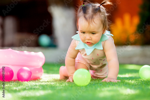 Toddler girl plays in summer with developing toys on green lawn.Toddler girl plays in dry pool