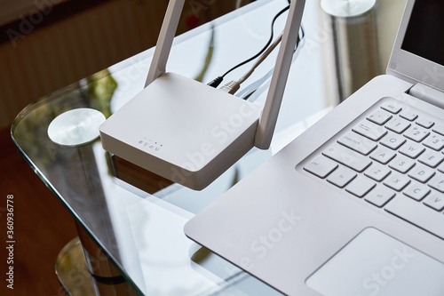 Fotografie White wireless wi-fi router near a laptop on a glass table