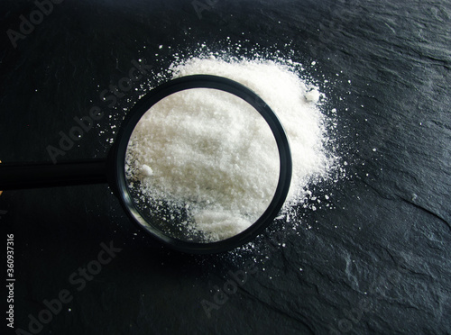 a white handful of salt on a black stone surface. View salt through a magnifying glass.