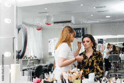 Fototapeta Naklejka Na Ścianę i Meble -  In a beautiful, modern beauty salon, a professional makeup stylist makes makeup for a young girl. Beauty, and fashion