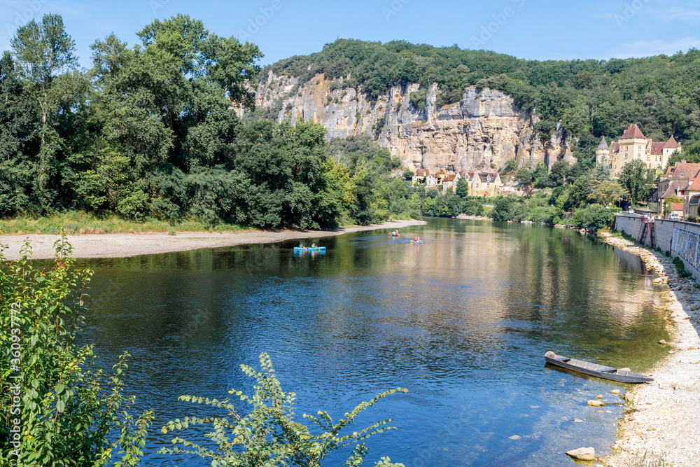 La Roque Gageac, one of France's most beautiful villages by the Dordogne River, backed by a steep hill / cliff, Malartrie Castle in the background, kayakers on the river. Travel France. La Roque Gageac, one of France's most beautiful villages by the Dordogne River, backed by a steep hill / cliff, Malartrie Castle in the background, kayakers on the river. Travel France.