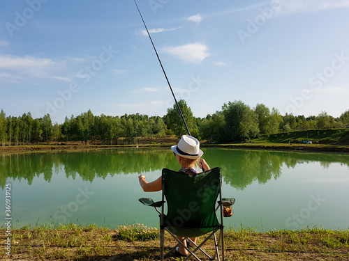 Girl in a hat on the lake alone catches a fish for fishing rod.
