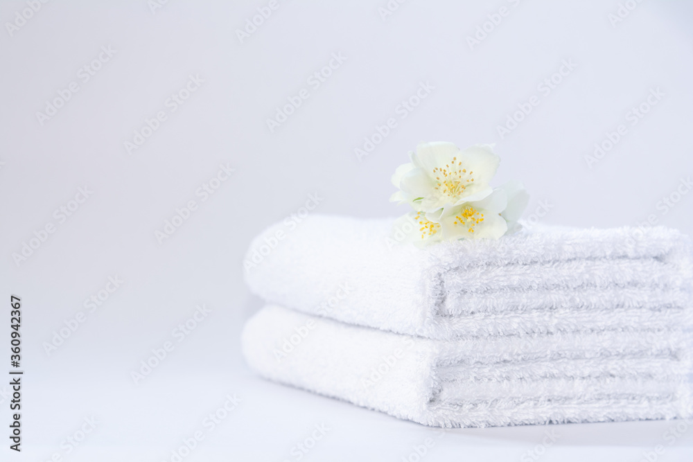Two white neatly folded terry towels with a jasmine flower on a light background. Two white neatly folded terry towels with a jasmine flower on a light background.