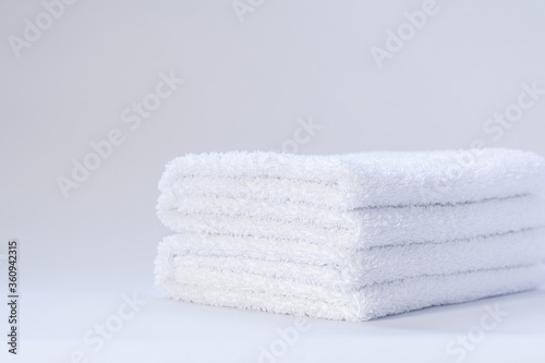 View of a stack of white folded terry towels on a light background.