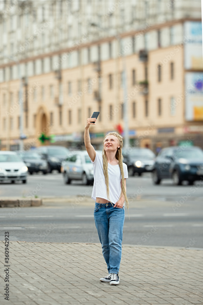 girl with long hair in dreadlocks takes  selfie in  city, cityscape with cars on background