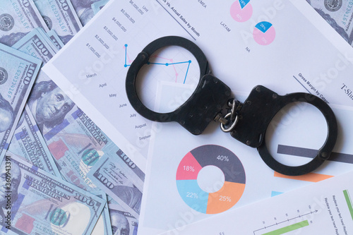 top view handcuffs against the background of charts and hundred-dollar bills