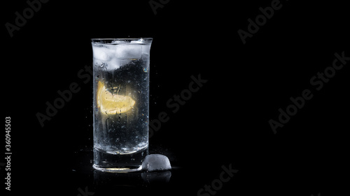 Refreshing full glass of water with a lemon slice and ice cubes isolated on black background