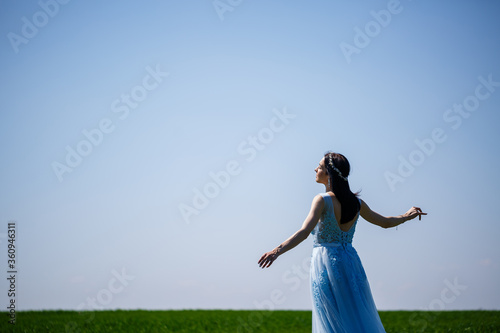 Young woman in a blue long dress on a background of green field. Fashion portrait of a beautiful girl with a smile on her face