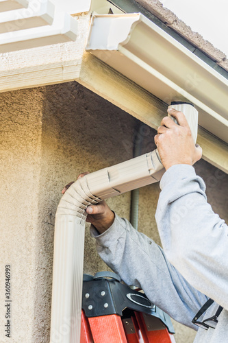 Worker Attaching Aluminum Rain Gutter and Down Spout to Fascia of House photo