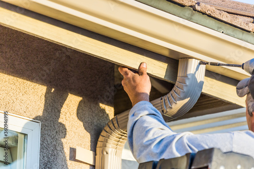 Worker Attaching Aluminum Rain Gutter and Down Spout to Fascia of House photo