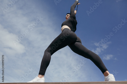 The photo below the girl performs the athletic workout against the cloudy morning sky. The athlete with an elastic rubber band.