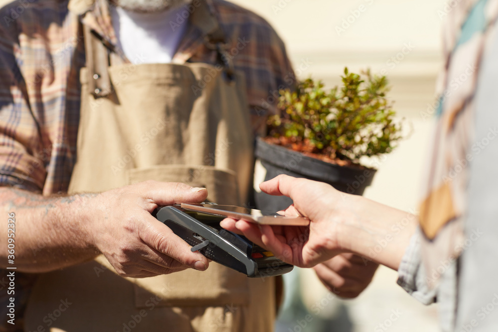 Close up of unrecognizable female customer holding bank card while paying via NFC in plantation outdoors, copy space