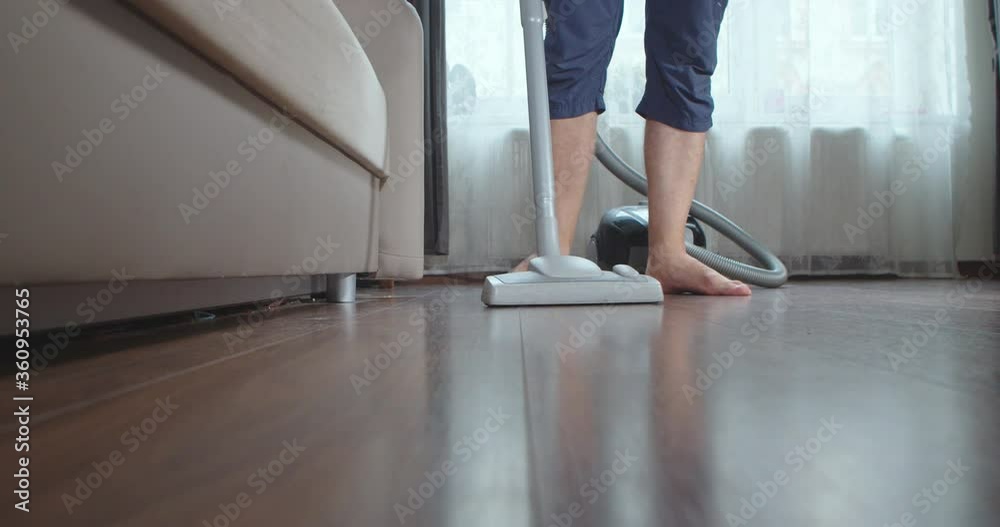 Young man doing housework with a vacuum cleaner in his hand. A man vacuums in a bright room early in the morning at the weekend.