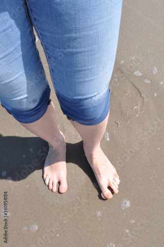 Barefoot wet female feet with a band-aid on toes in wet jeans on the sand, shot from above