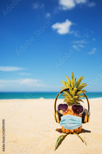 Ripe attractive pineapple wearing face mask because of Air pollution or virus epidemic in the world. On the sand against turquoise sea. Summer vacation concept during an epidemic. New reality