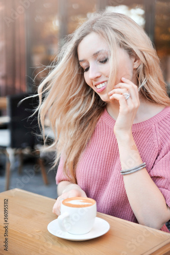 Beautiful young woman posing in caffeine with cup of latte.