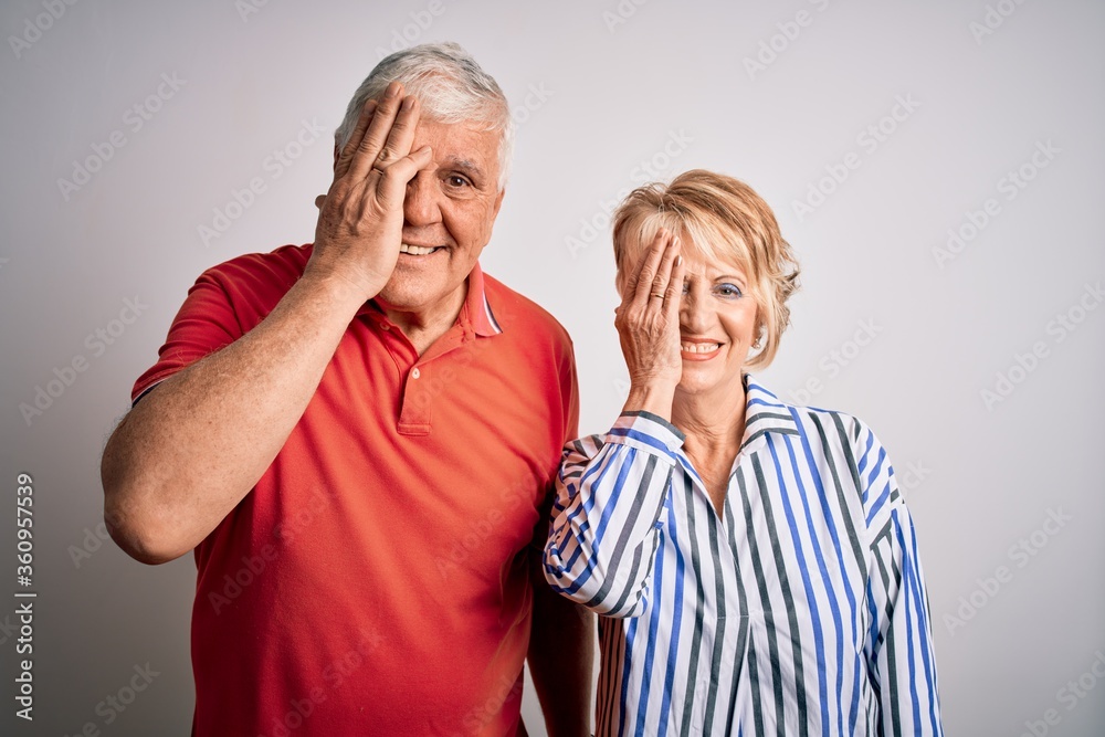 Senior beautiful couple standing together over isolated white background covering one eye with hand, confident smile on face and surprise emotion. Senior beautiful couple standing together over isolated white background covering one eye with hand, confident smile on face and surprise emotion.