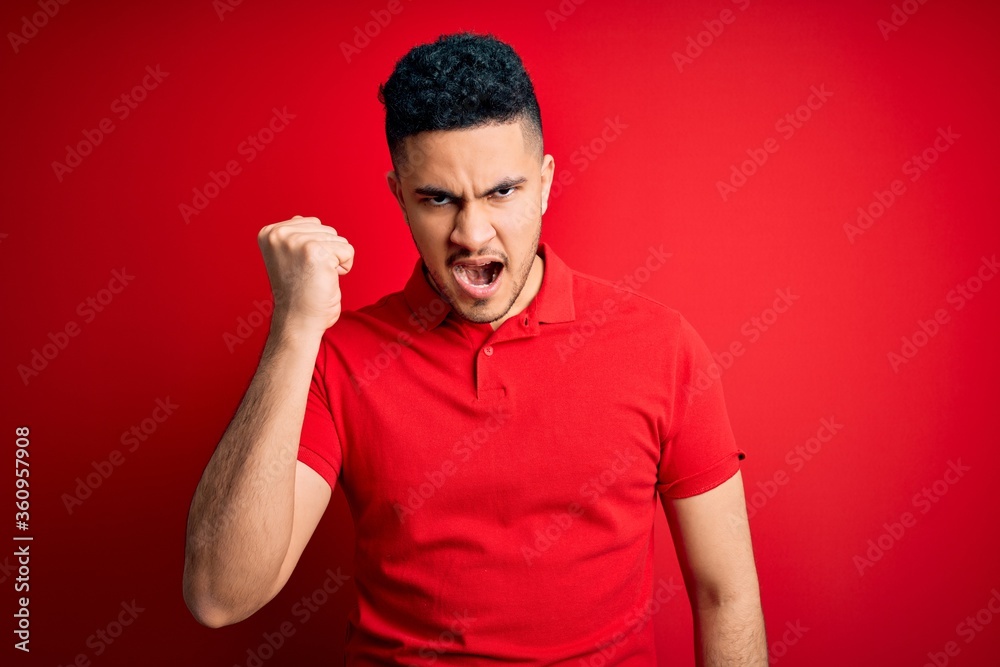 Young handsome man wearing red casual polo standing over isolated background angry and mad raising fist frustrated and furious while shouting with anger. Rage and aggressive concept. Young handsome man wearing red casual polo standing over isolated background angry and mad raising fist frustrated and furious while shouting with anger. Rage and aggressive concept.