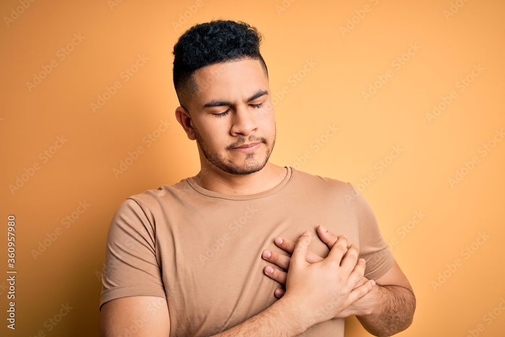 Young handsome man wearing casual t-shirt standing over isolated yellow background smiling with hands on chest with closed eyes and grateful gesture on face. Health concept. Young handsome man wearing casual t-shirt standing over isolated yellow background smiling with hands on chest with closed eyes and grateful gesture on face. Health concept.