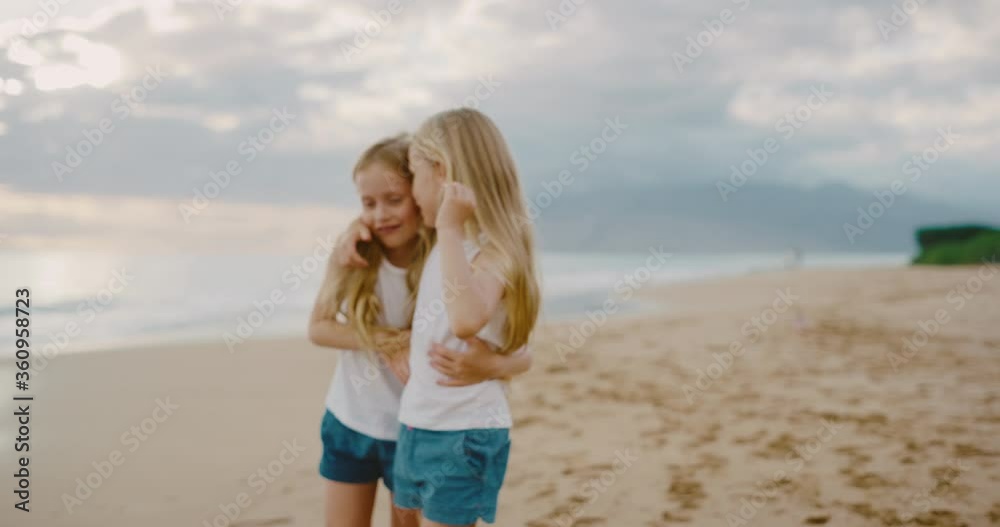 Happy young twin girls walking down the beach playing at sunset, summer family lifestyle Happy young twin girls walking down the beach playing at sunset, summer family lifestyle