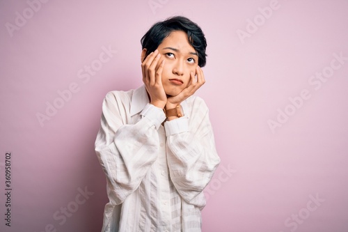 Young beautiful asian girl wearing casual shirt standing over isolated pink background Tired hands covering face, depression and sadness, upset and irritated for problem © Krakenimages.com
