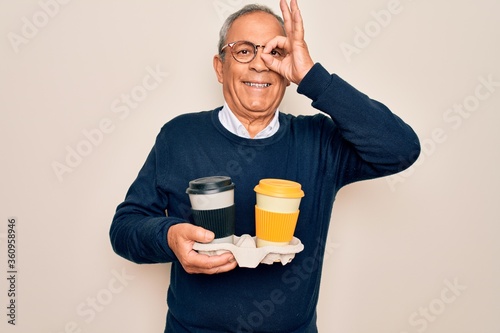 Senior handsome hoary man holding tray with takeaway cups of coffee over white background with happy face smiling doing ok sign with hand on eye looking through fingers