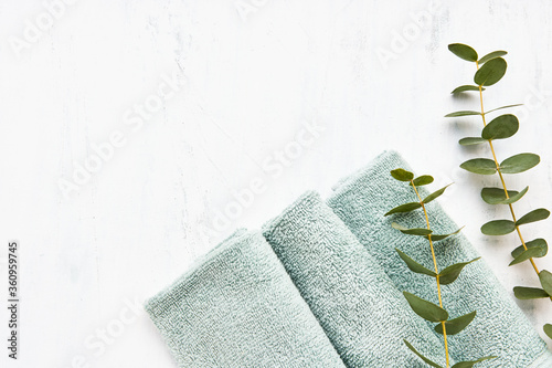 Rolled fluffy towel and green eucalyptus branch on white background. Minimalist scandinavian style. Hygiene, wellness well-being, body care concept. Copy space