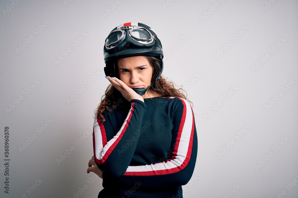 Beautiful motorcyclist woman with curly hair wearing moto helmet over white background thinking looking tired and bored with depression problems with crossed arms. Beautiful motorcyclist woman with curly hair wearing moto helmet over white background thinking looking tired and bored with depression problems with crossed arms.