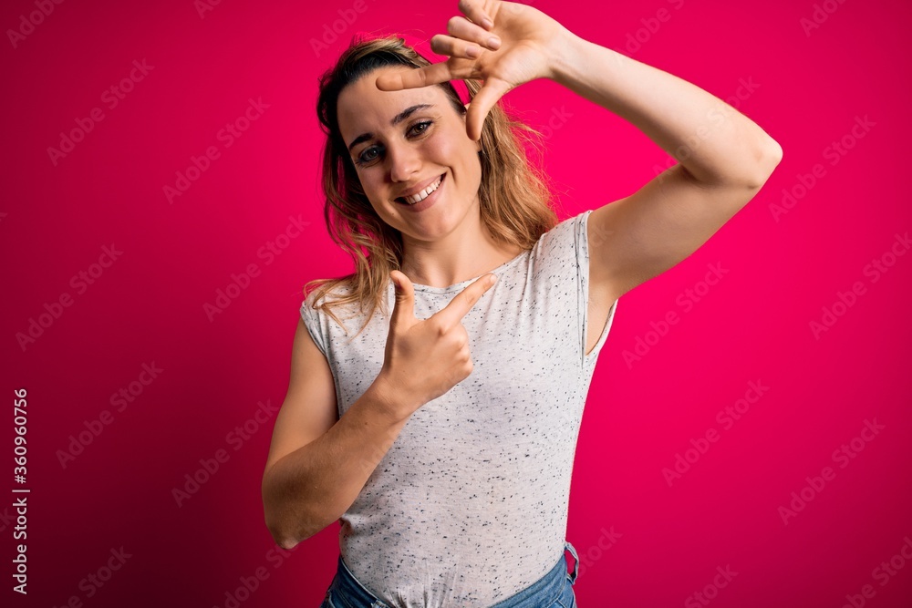 Young beautiful blonde woman wearing casual t-shirt standing over isolated pink background smiling making frame with hands and fingers with happy face. Creativity and photography concept.