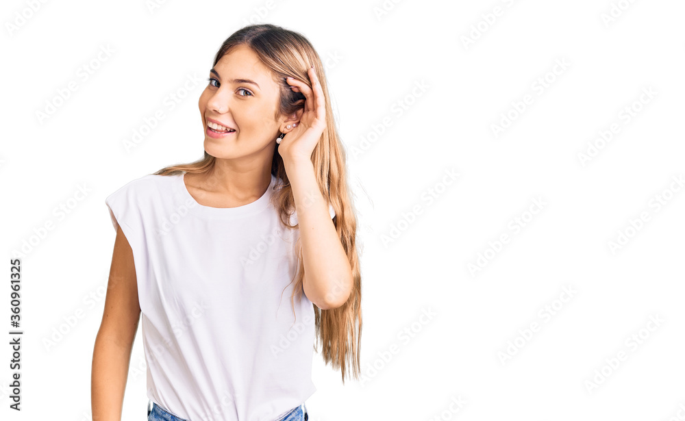 Beautiful caucasian woman with blonde hair wearing casual white tshirt smiling with hand over ear listening an hearing to rumor or gossip. deafness concept. Beautiful caucasian woman with blonde hair wearing casual white tshirt smiling with hand over ear listening an hearing to rumor or gossip. deafness concept.