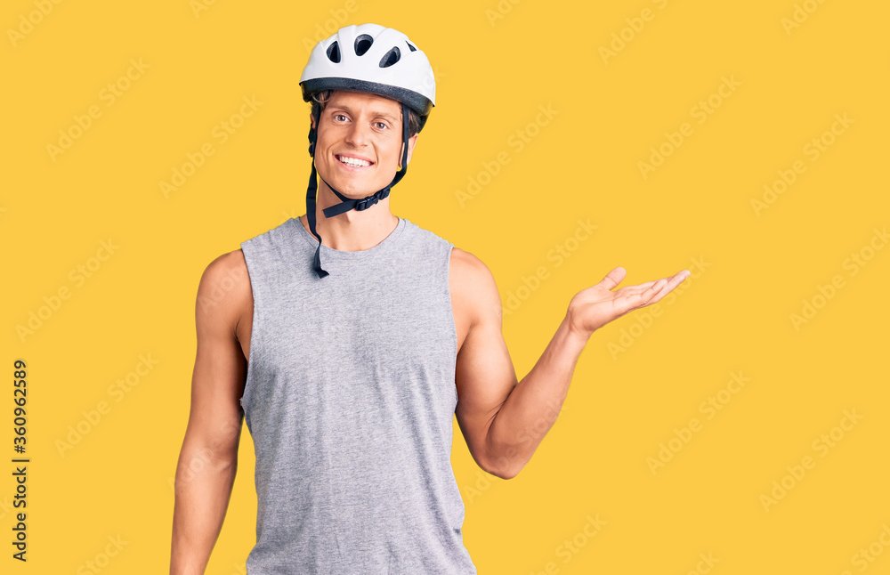 Young handsome man wearing bike helmet smiling cheerful presenting and pointing with palm of hand looking at the camera.