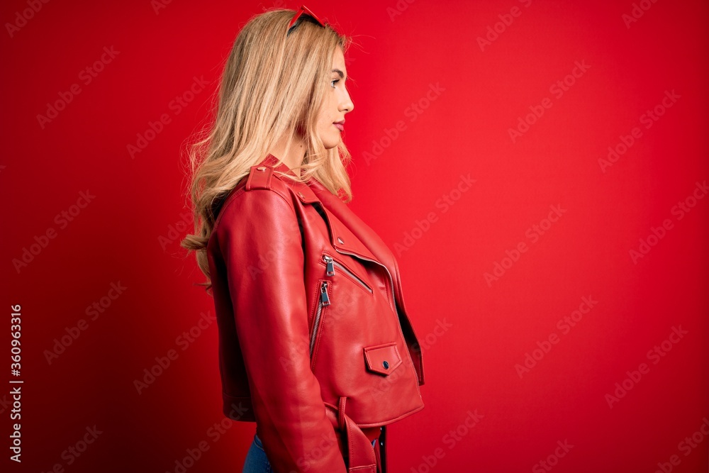 Young beautiful blonde woman wearing casual jacket standing over isolated red background looking to side, relax profile pose with natural face with confident smile. Young beautiful blonde woman wearing casual jacket standing over isolated red background looking to side, relax profile pose with natural face with confident smile.