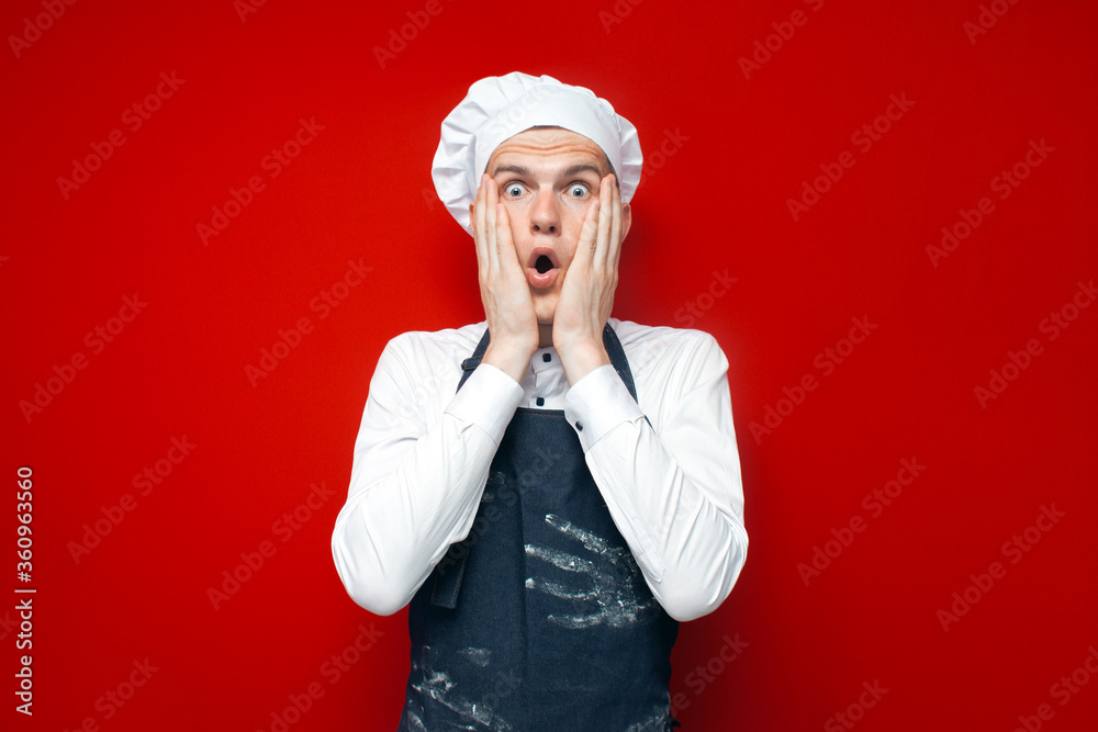 shocked chef cook surprised at red isolated background, kitchen worker in uniform with kitchen items in stress