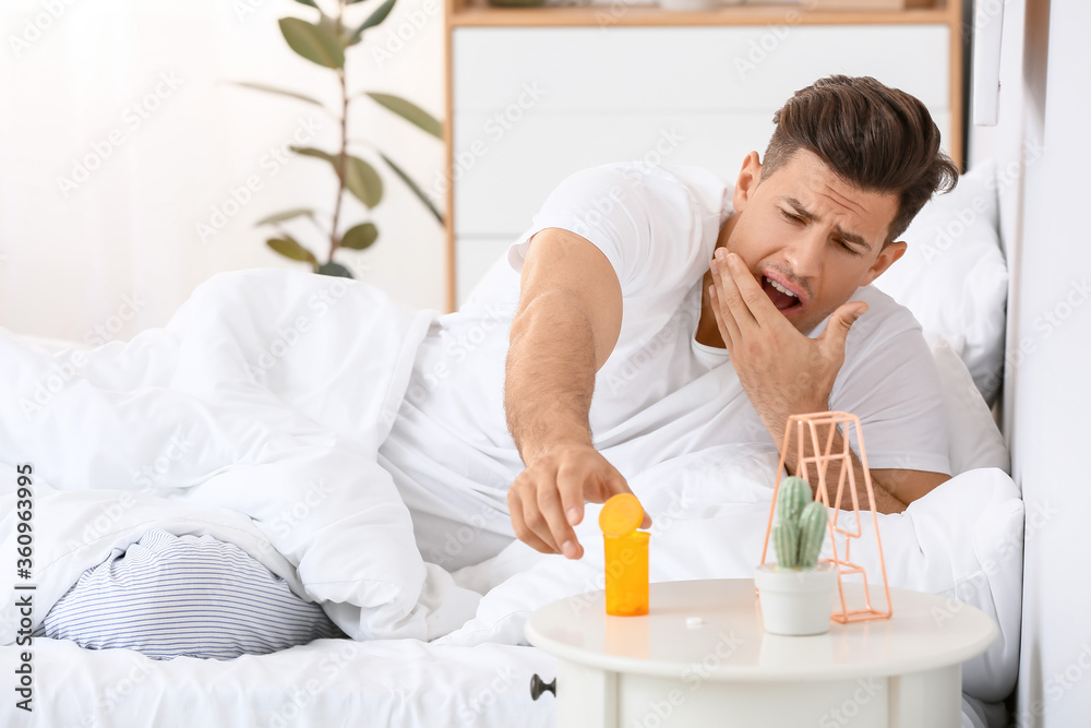 Young man taking sleeping pills in bedroom Young man taking sleeping pills in bedroom