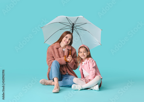 Mother and little daughter with umbrella on color background