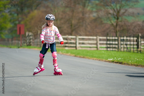 A young girl on roller blades and wearing protective equipment skates along a country road