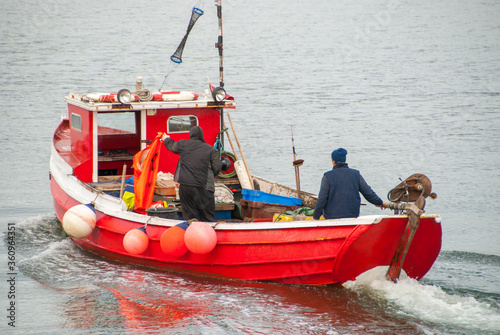 Two fishermen aboard a moving small red fishing boat